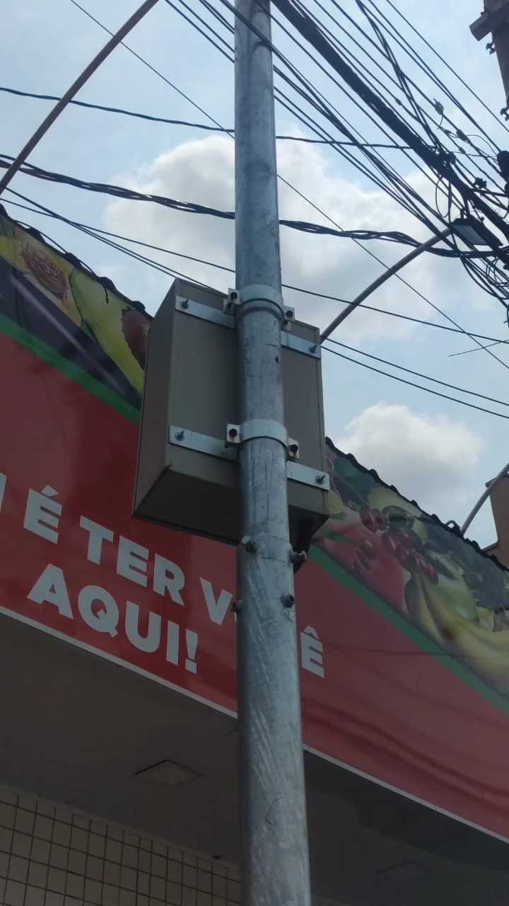 Detalhe de caixa fixada ao corpo do poste por abraçadeiras